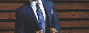 Man's torso wearing a blue suite standing in front of a wood background.