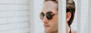 Close up of mans face wearing sunglasses with a neutral expression.