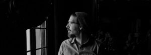 black and white photo of man (zachary nelson) looking out a window to the left.