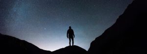 Man standing on a mountain scape with a stary sky.