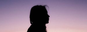 Silhouette of girl's side profile facing the right with pink & purple back ombre background.