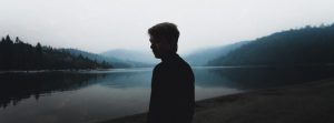 Man standing in front of a lake and mountain nature view.
