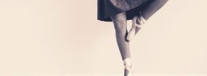 Pointe dancer photographed from the thighs down in a figure 4 position.