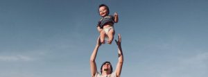 Male throwing a baby in the air smiling outside.