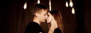 Male and female close to kissing under lights.