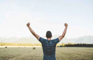 man holding arms up in victory in field by mountains.