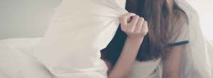 Women in bed pulling pillow over her face.