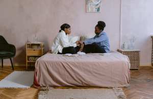 Two women sitting cross legged on bed holding hands