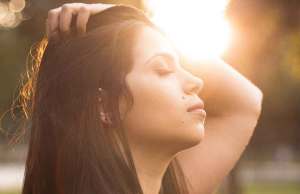 Woman running her hand through her hair closing her eyes face to the sun.