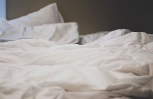 an unmade bed with white pillows and blankets.