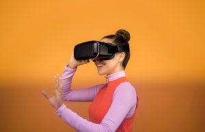 woman enjoying her virtual reality goggles in front of a orange background.
