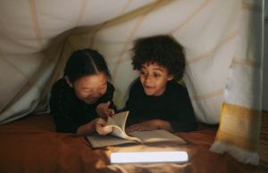 Two kids reading inside of a tent smiling.