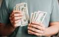 man-holding-dollar-bills-in-hands-with-green-shirt