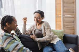 Mother and daughter laughing and talking on a gray couch