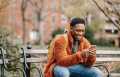 Delightful African American man surfing modern cellphone in city park