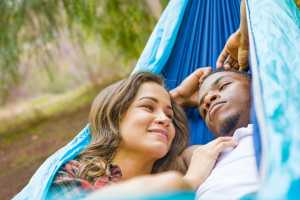 Woman and man cuddling in a blue hammock outdoors