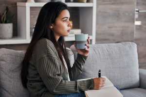 Woman on a gray couch drinking tea and journaling